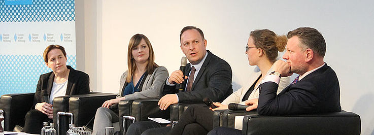 Panel auf der Bühne. Sitzend. Im Hintergrund HSS-Rollup