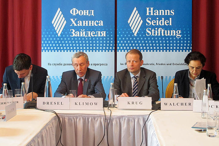 Vier Personen an einem Konferenztisch vor Stellwänden auf deutsch und russisch mit dem Logo der Hanns-Seidel-Stiftung