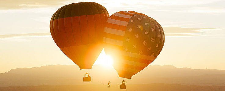 Zwei Fesselbalons aneinander in der Luft. Der rechte mit den stars und stripes der amerikanischen Flagge, der linke mit der Deutschlandflagge bemalt.
