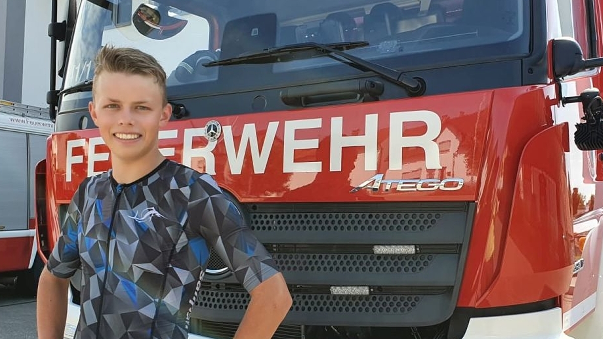 Held steht lächelnd vor einem großen Feuerwehrauto.