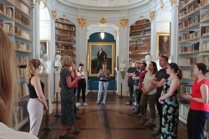 Eine Menschengruppe in einem Raum mit vielen antiken Büchern, die bis zur Decke reichen