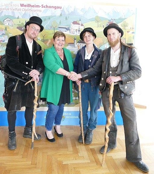 Landrätin Andreas Jochner-Weiß steht in der mitte zwischen einer Handwerkerin und zwei Handwerkern. Letztere Tragen die traditionelle Tracht der Walz samt Wanderstab. Alle lächeln in die Kamera.