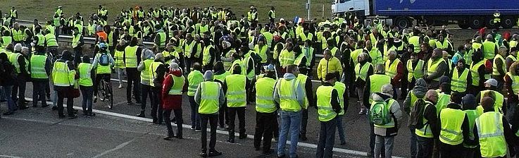 Etwa 200 Menschen mit gelben Warnwesten haben sich auf einem Parkplatz versammelt.