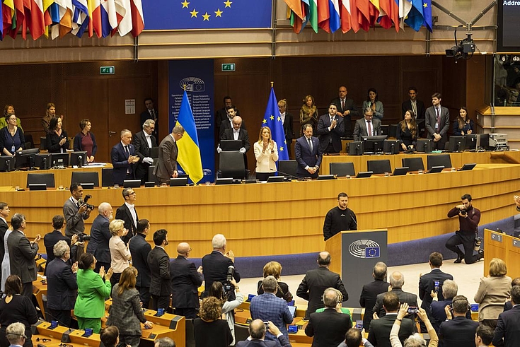 Selenskyj am Rednerpult des Europäischen Parlaments. Über ihm Europäische Flaggen, Menschen klatschen ihm Beifall.