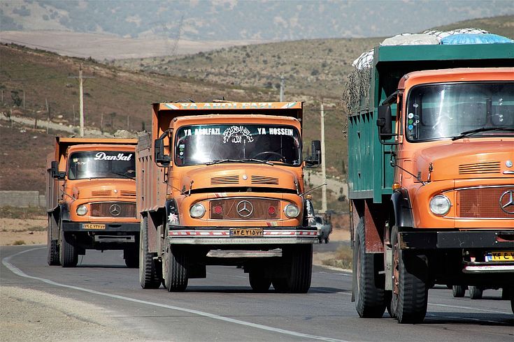 Drei Lastwägen, hochbeladen, auf einer Straße in einer Wüstenlandschaft, die auch Ausrüßtung transportieren könnten.