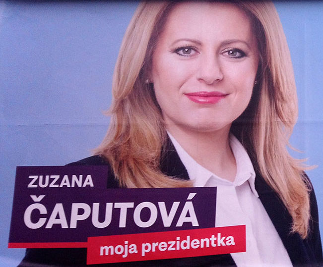 Attraktive Frau mit ordentlicher Bluse, Blazer und offenen Haaren und entschlossenem Blick schaut von einem schlichten Wahlplakat.