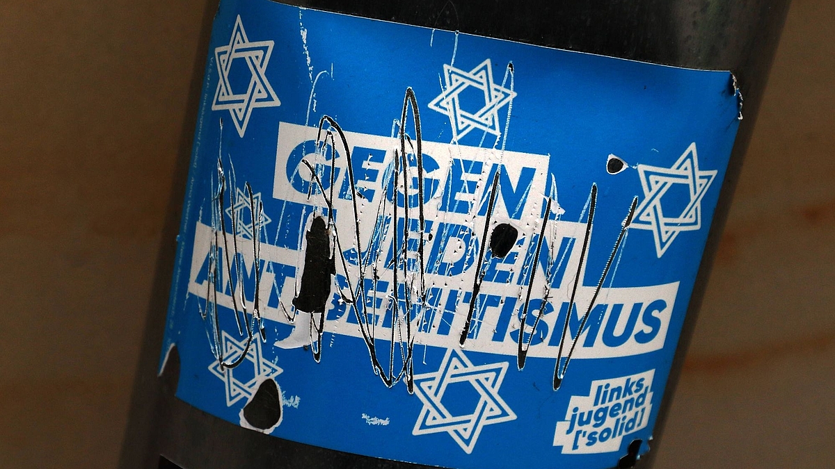 Politische Botschaft gegen Antisemitismus an einer Laterne in Form eines beschädigten Stickers. Der Schriftzug wurde offenbar von politisch Andersdenkenden mit einem spitzen Gegenstand beschädigt.