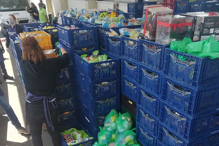 Freiwillige sortiert Lebensmittel aus großen, gestapelten Kisten aus