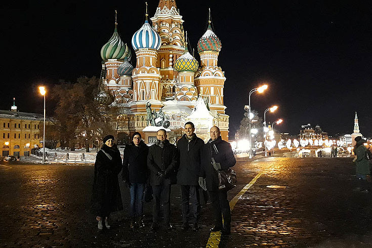 Vor den berühmten russischen Zwibeltürmen stehen die fünf genannten bei Nacht auf dem roten Platz und lächeln in die Kamera.