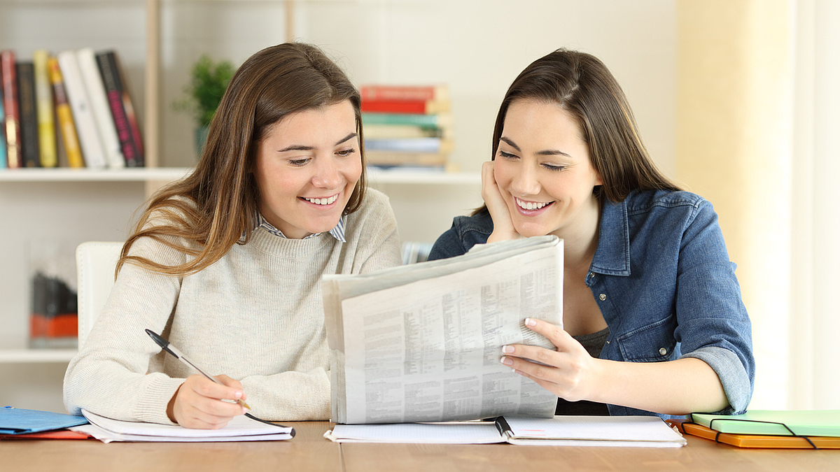 Zwei junge Frauen lesen gemeinsam eine Zeitung