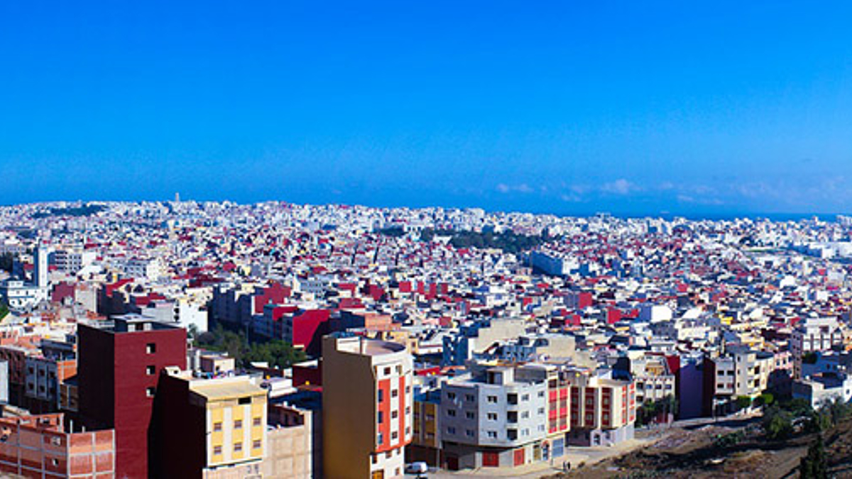 Die Stadt Tanger, flache, niedrige Gebäude unter einem wolkenlosen Himmel. Im Hintergrund lässt sich das Meer erahnen.