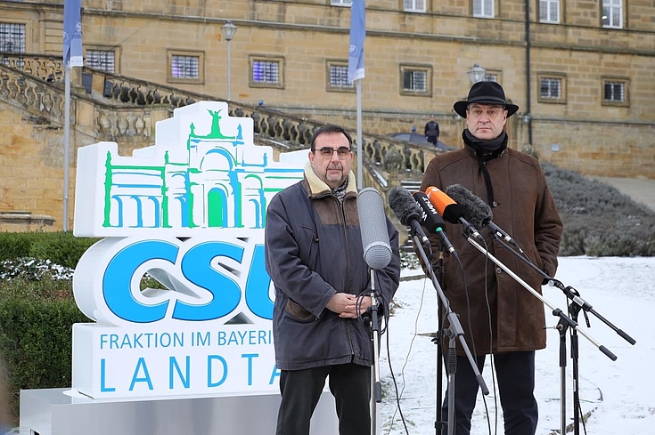 Die beiden stehen vor der großen Treppe im Innenhof von Kloster Banz und halten eine Pressekonferenz. Söder hat einen Hut auf.