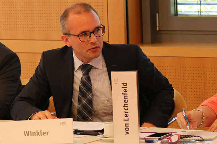 Besorgter Blick bei Wortbeitrag. Dunkler Anzug, schütteres Haar, karierte Krawatte