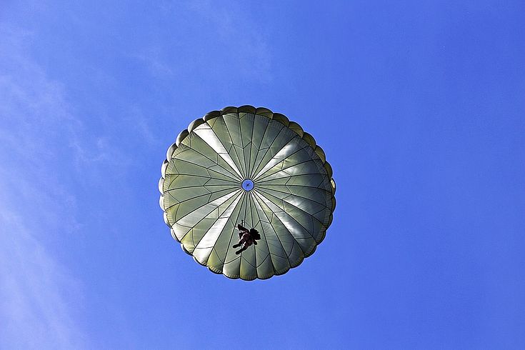 Ein Fallschirm mit Soldat von unten. Darüber der Himmel