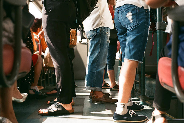 Beine in unerschiedlichen Hosen stehen in einem Straßenbahnabteil. Es scheint sehr voll zu sein.