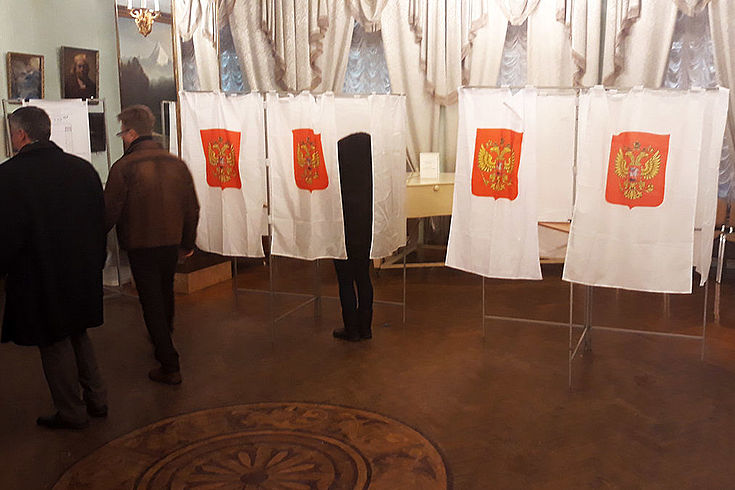 Raum mit mit Vorhängen verhangenen Wahlkabinen auf denen das russische Wappen prangt.