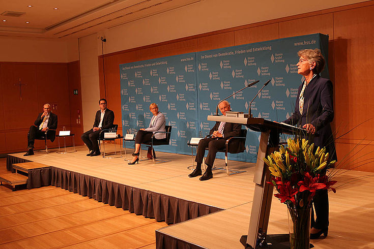 Breit-Keßler steht am Rednerpult. Hinter ihr sitzen die anderen Gäste auf dem Podium.
