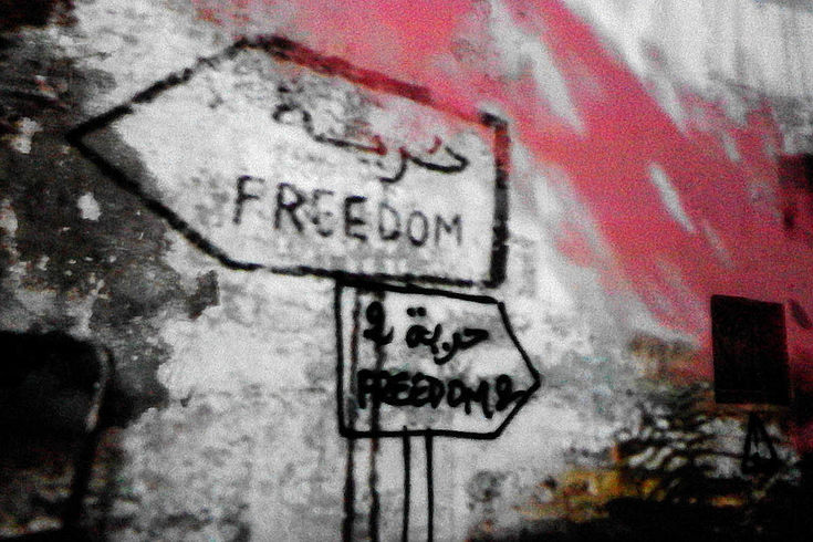 Grafitto eines Wegweisers der in zwei verschiedene Richtungen zeigt. Darauf ist mit arabischen und römischen Buchstaben "Freedom" geschrieben. 