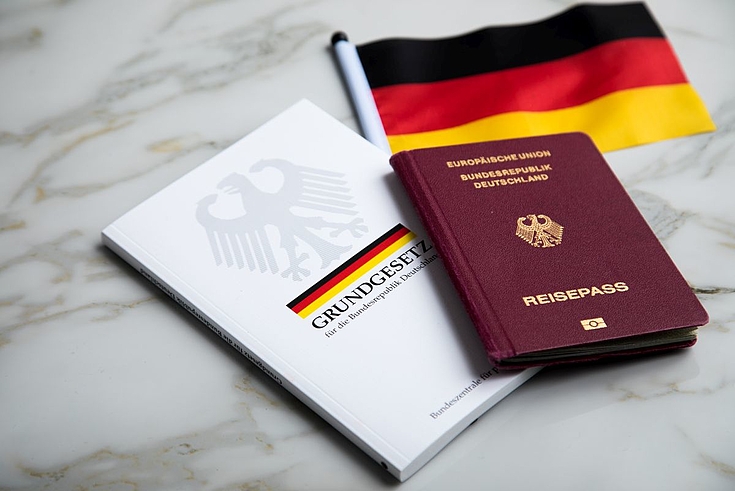 Auf dem Bild liegt auf einem Tisch ein deutscher Pass neben dem Grundgesetz und einer deutschen Flagge.