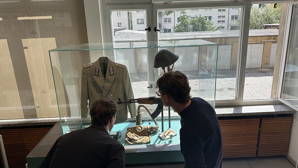 Stipendiaten betrachten in einem Schaukasten ein Kalaschnikow-Sturmgewehr und eine Uniform