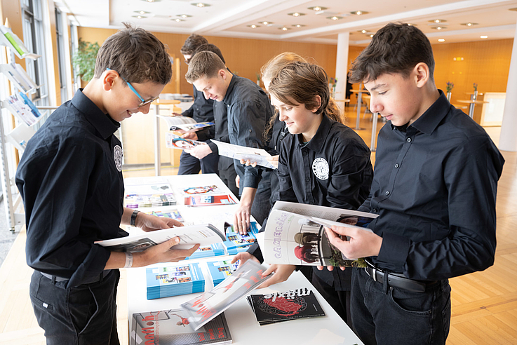 Schülerinnen und Schüler schauen sich die ausgelegten Schülerzeitungen der verschiedenen Schulen an, die am diesjährigen Wettbewerb teilgenommen haben.