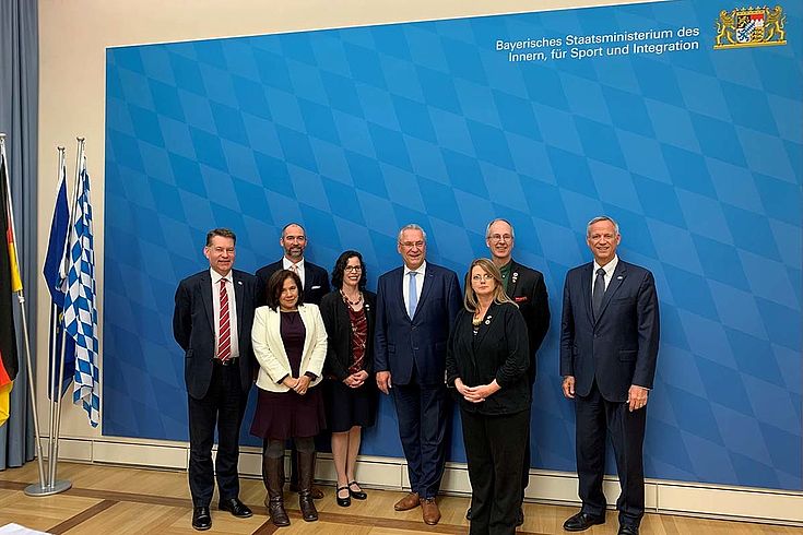 Gruppenbild vor einer sehr großen Stellwand des Bayerischen Innenministeriums