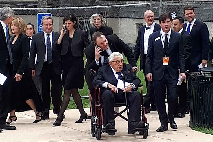 Kissinger wird im Rollstuhl von einem Bodyguard in Richtung Capitol geschoben. 