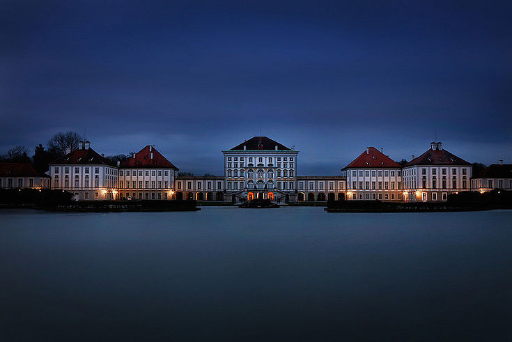 Schloss Nymphenburg bei Nacht jenseits eines kleinen Sees 