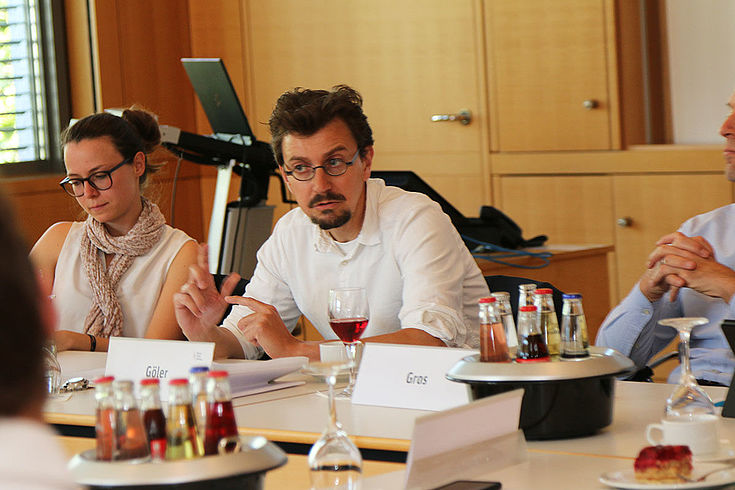 Junger Professor erklärt, sitzend. Brille, Hemd.