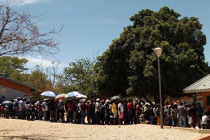 Vor einem flachen Gebäude in Namibia steht eine lange Schlange von wartenden Menschen, die zur Wahl gehen