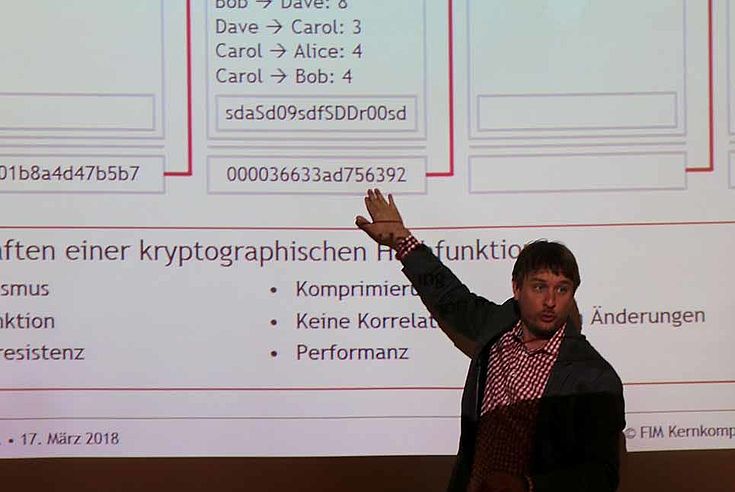 Präsentator deutet auf eine Zeile in einem Schaubild zum Thema Blockchain