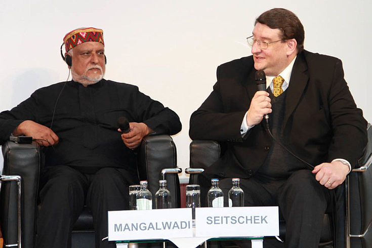 Seitschek, ein untersetzter Mann mit runder Brille spricht mit freundlichem Gesicht ins Mikorfon. Neben ihm sitzt  Dr. Vishal Mangalwadi mit orientalisch anmutender Kopfbedeckung.