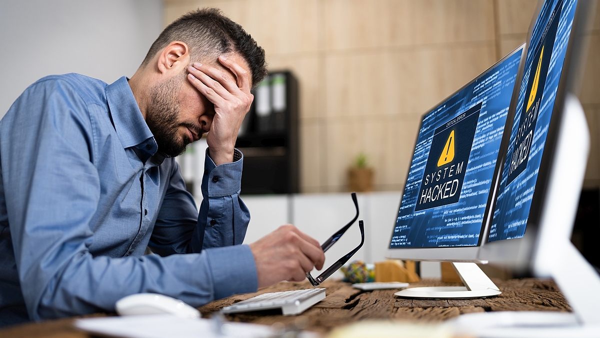 Ein Firmenmitarbeiter sitzt verzweifelt am Rechner. Er wurde Opfer eines Hackerangriffs.