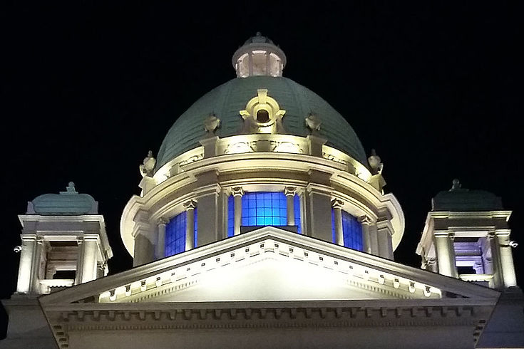Teilansicht des Parlamentsgebäudes in Belgrad bei Nacht mit erleuchteten Fenstern in der Kuppel