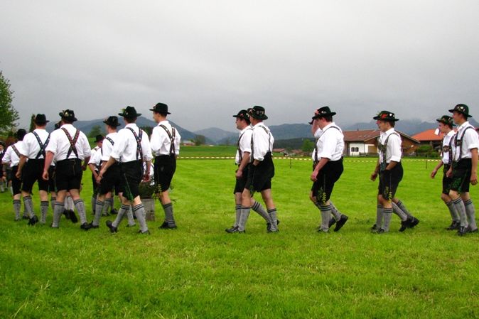 Eine Gruppe junger Männer in bayerischer Tracht im Gänsemarsch auf einer Wiese