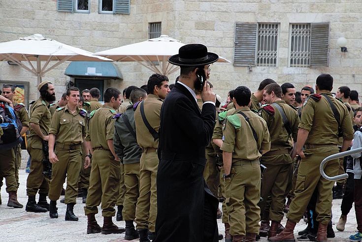 Orthodoxer Jude mit Handy am Ohr geht an einer Gruppe Soldaten vorbei.