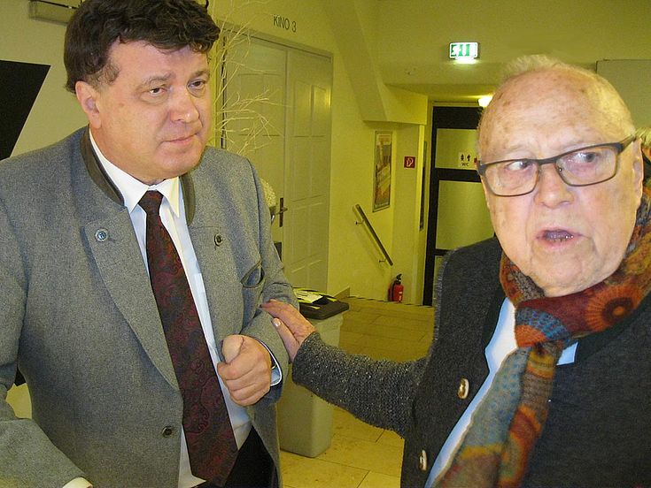 Vilsmaier dreht sich nach rechts und fasst den links neben ihm stehenden Arthur Kolbe am Arm, als wolle er ihn auf etwas hinweisen.