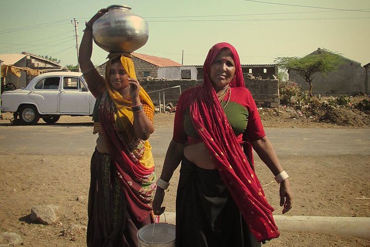 Zwei Frauen mit Krügen voller Wasser auf einer staubigen Straße