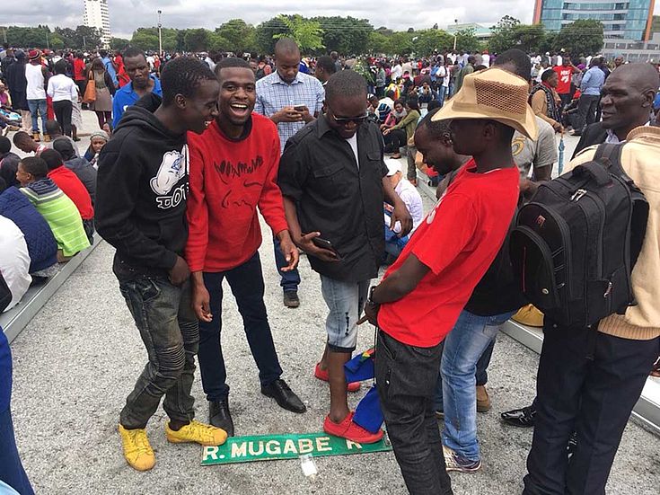 Junge Demonstranten treten auf ein Straßenschild mit Mugabes Namen und freuen sich.