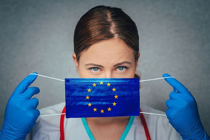 Eine Krankenschwester zieht sich einen Mundschutz mit den EU-Sternen an.