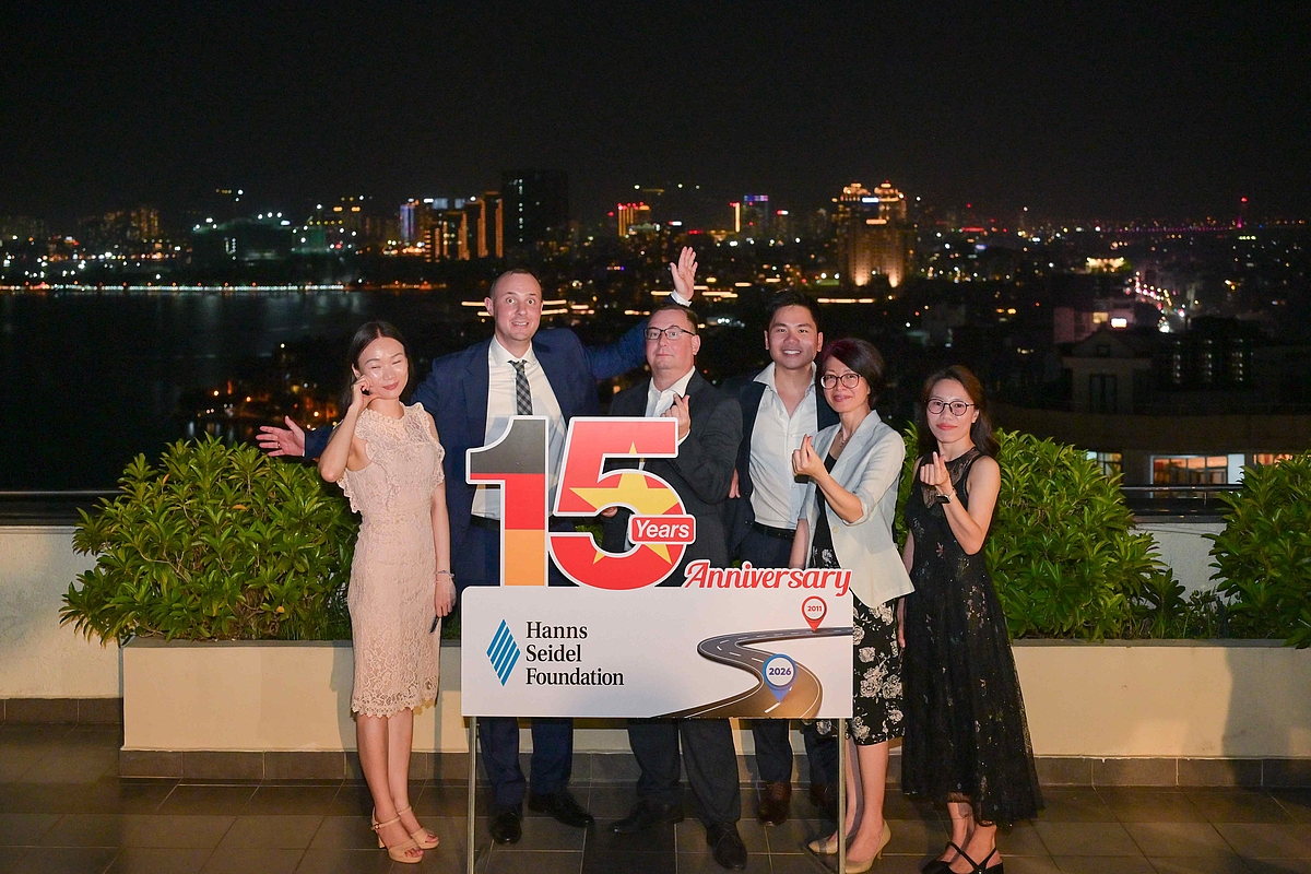 Das Team steht in festlicher Kleidung auf der Dachterrasse mitten in Hanoi. In der Mitte von Ihnen ist das Logo des 15-jährigen Bestehens zu sehen.