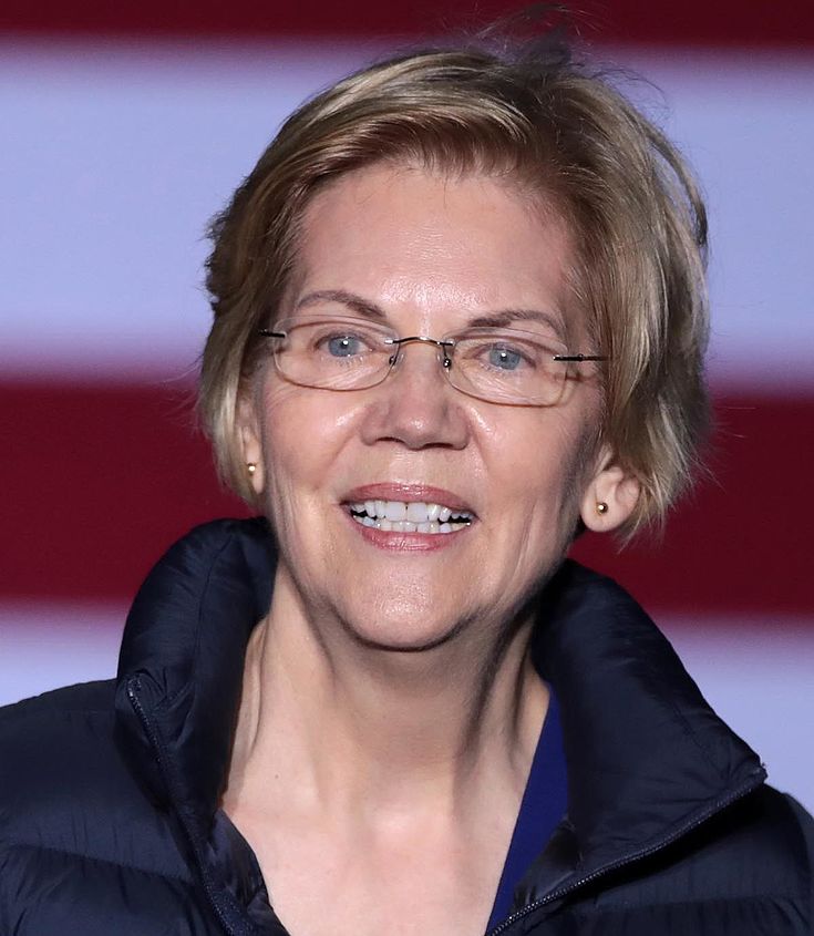 Warren lächelt in die Kamera. Dahinter US-Flagge