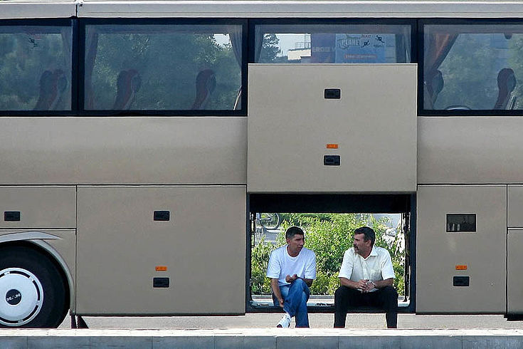 Zwei Männer sitzen in der offenen Gepäcktür eines Reisebusses und reden miteinander.
