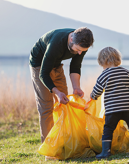 Kind mit Vater sammelt Müll, im Hintergrund See und Berge