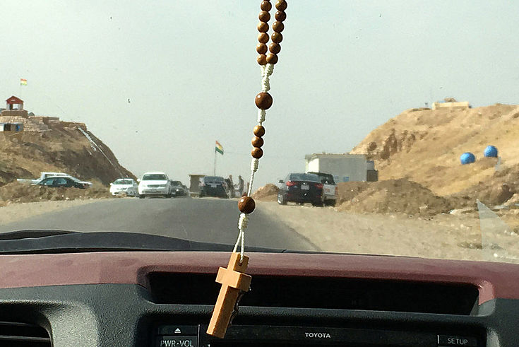 Ein Kreuz hängt von dem Rückspiegel eines Autos, das auf den Checkpoint zufährt.