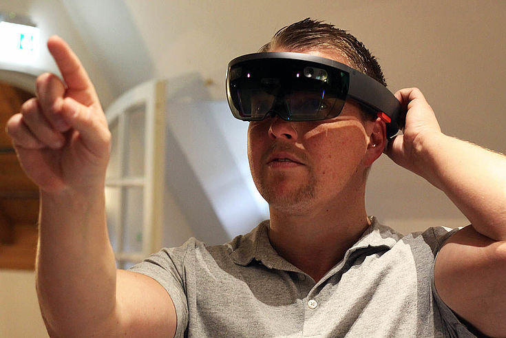 Junger Mann mit riesigen VR-Brille, der vor sich in die Luft deutet und offenbar gerade etwas bedient. 