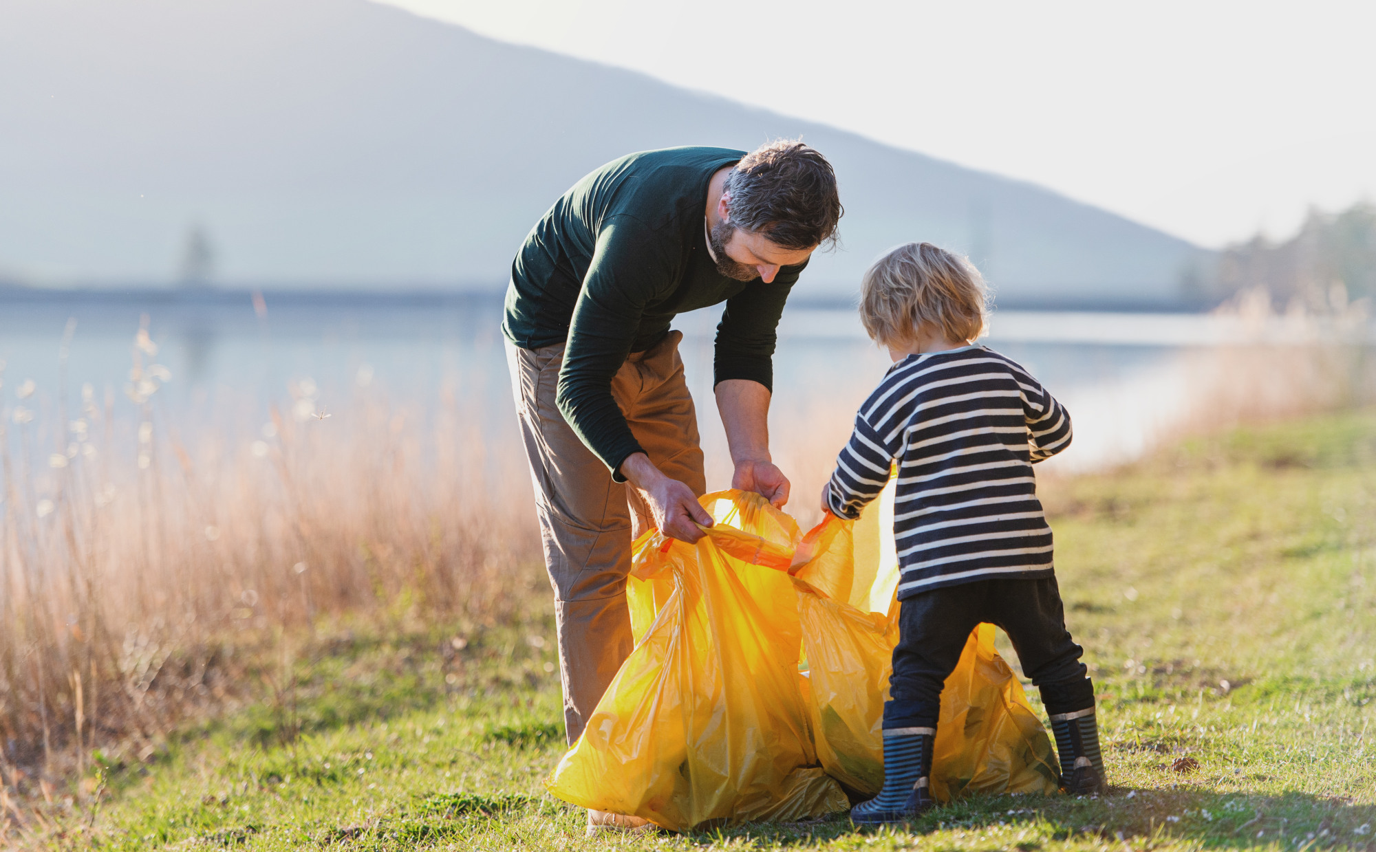 Kind mit Vater sammelt Müll, im Hintergrund See und Berge
